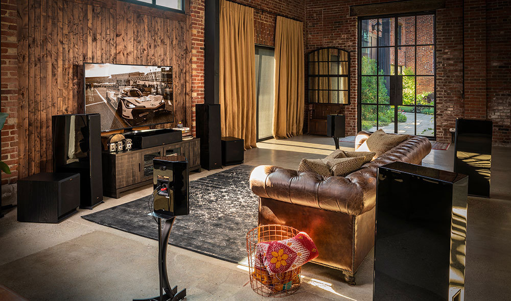 Luxury home theater setup with wall-mounted TV, surround sound speakers, and leather seating in a modern loft living room.